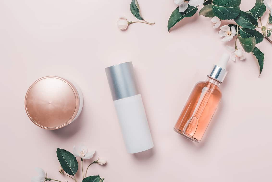 Pink natural cosmetics: oil, serum, cream, mask on the background with flowers. Flat lay, minimalism